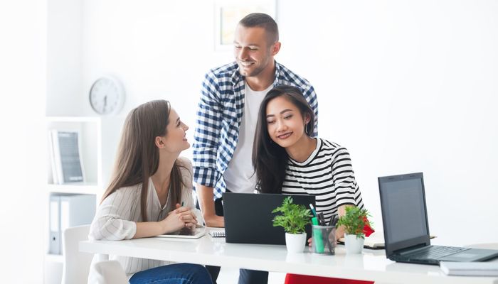 Smiling young businesswomen using laptop at meeting while discussing ideas with her business team