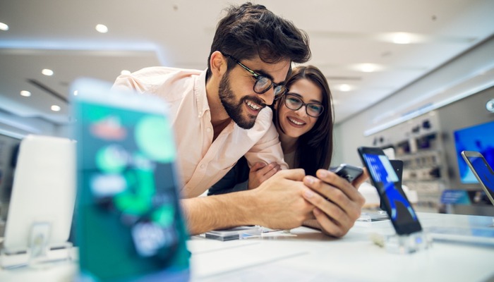 Close up focus view of a cheerful charming happy young student love couple choosing a new mobile in a tech store.