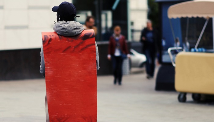 Man promoter with an advertising poster handing out flyers by urban streets