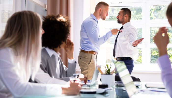 Stressed Businesspeople Sitting In Front Of Two Colleagues Fighting In Office