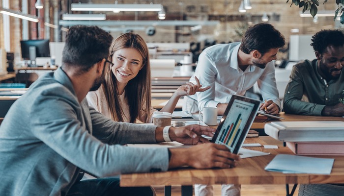 Group of young modern people in smart casual wear communicating and using modern technologies while working in the office