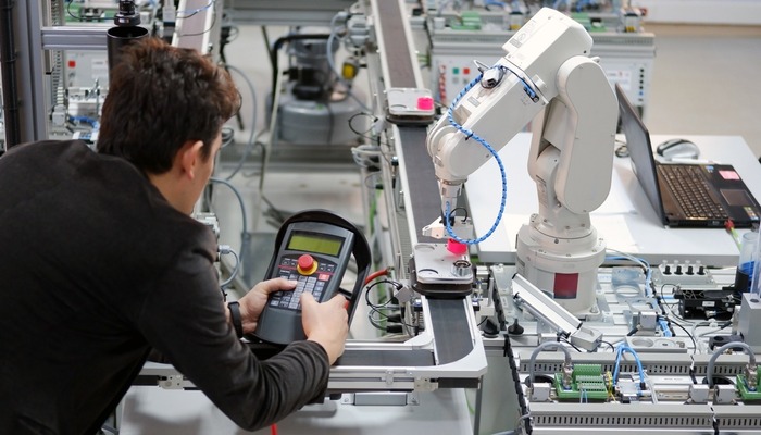 Man is holding teach panel to control a robotic arm which is integrated on smart factory production line. industry 4.0 automation line which is equipped with sensors and robotic arm.