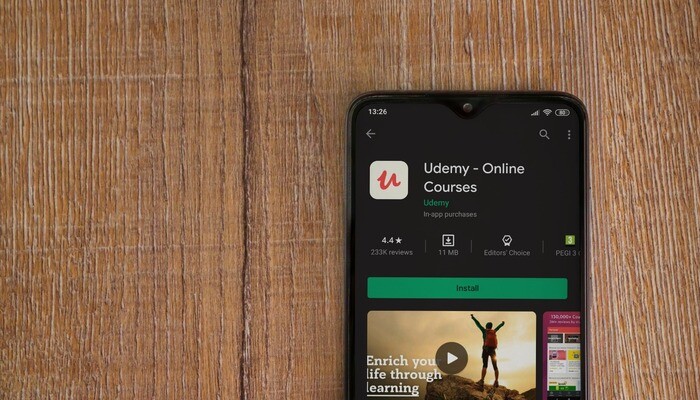 Udemy app play store page on the display of a black mobile smartphone on wooden background